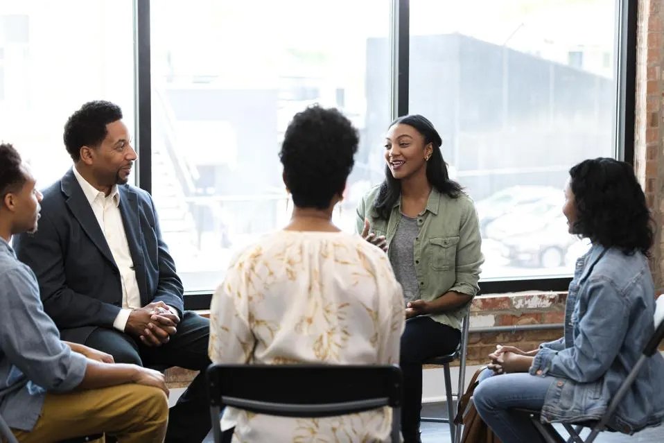 group of black people sitting on chairs in a circle discussing things